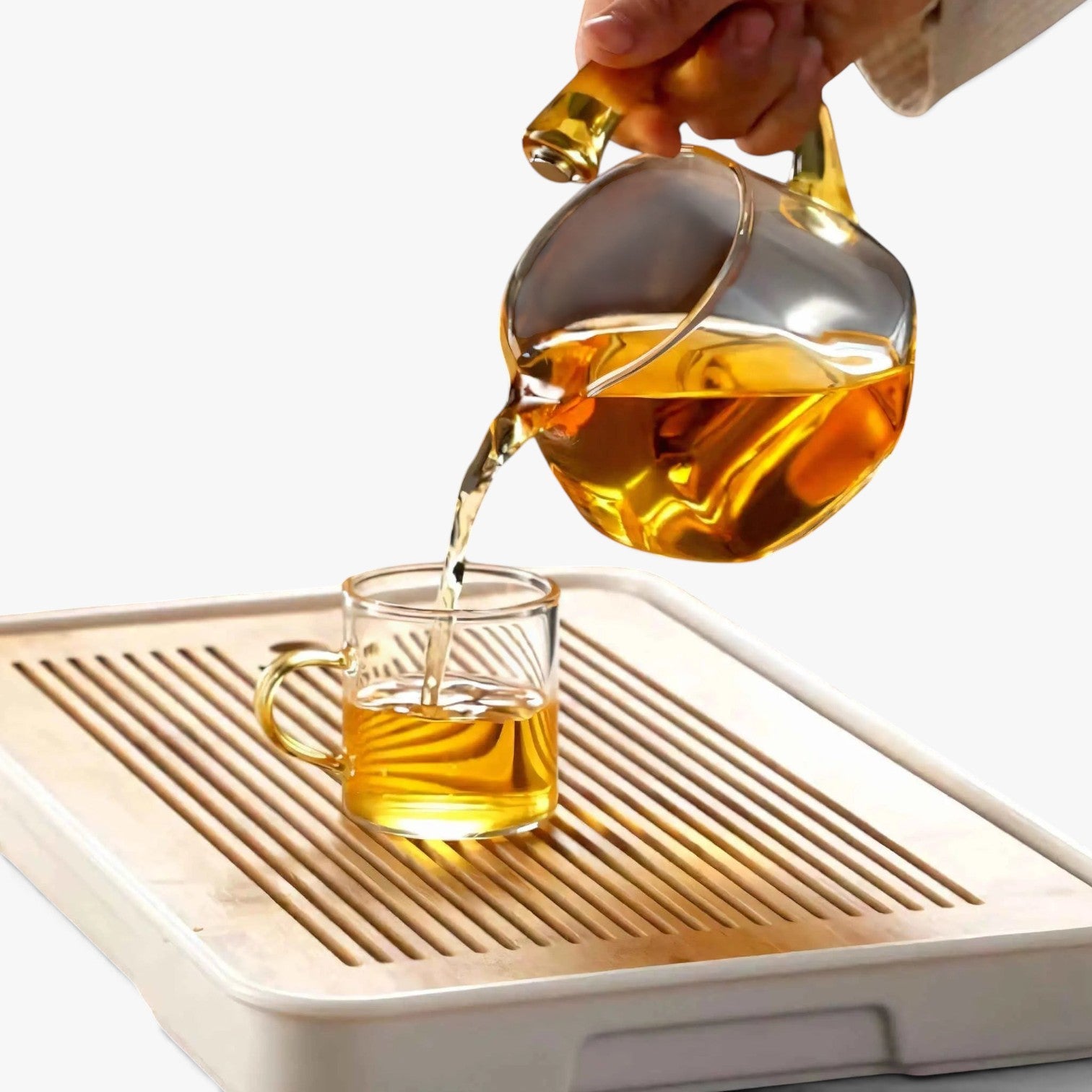Roselva TranquiliTea magnetic infuser teapot pouring golden tea into a matching glass cup on a wooden tea tray.